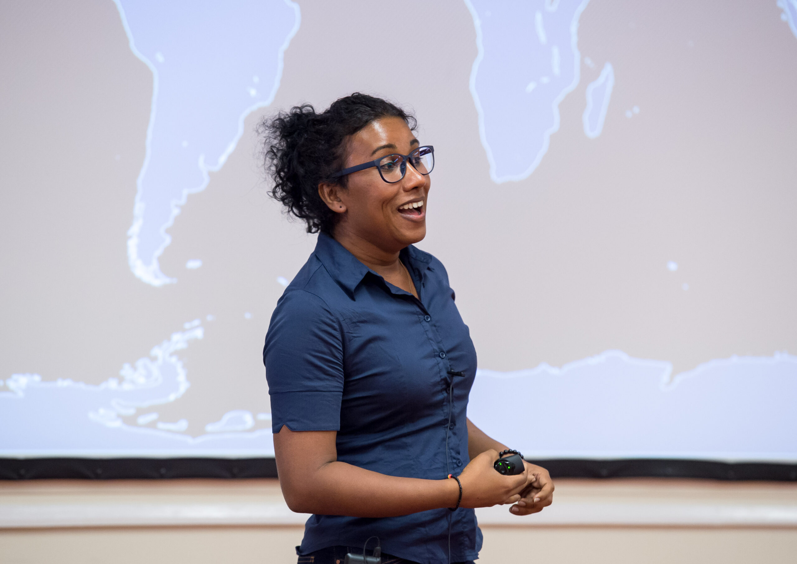 Izzy is wearing a blue shirt and glasses, and smiling and looking off camera towards an audience.