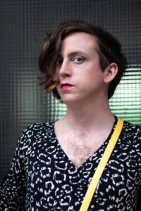 Juani is wearing a black and white animal print top, deep pink lipstick, and an undercut. She is looking at the camera.